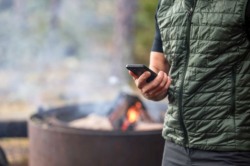 Man tittar på telefonen bredvid en eld utomhus.